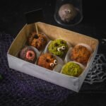 Decorative Halloween-themed truffles in a box with spooky designs and colorful coatings.